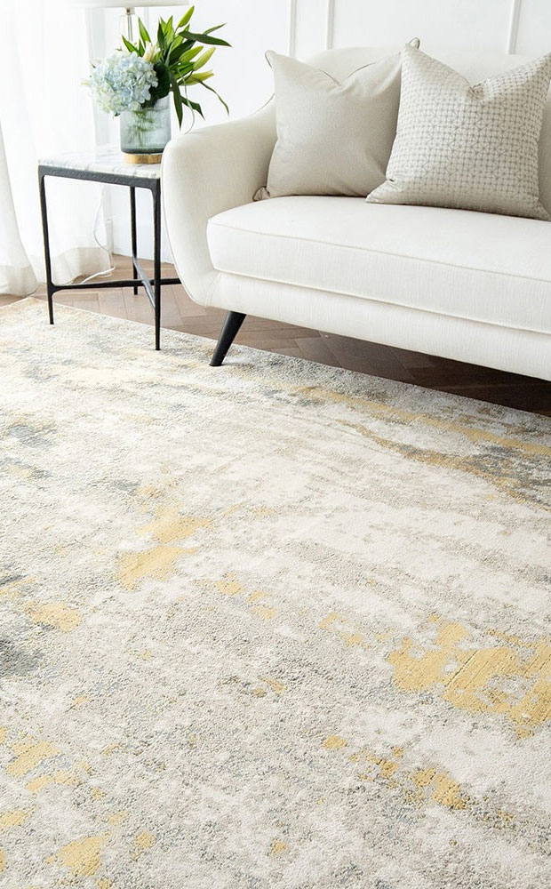 Aurora rug with grey and gold tones, styled in a bright living room with a white sofa and minimalist decor.