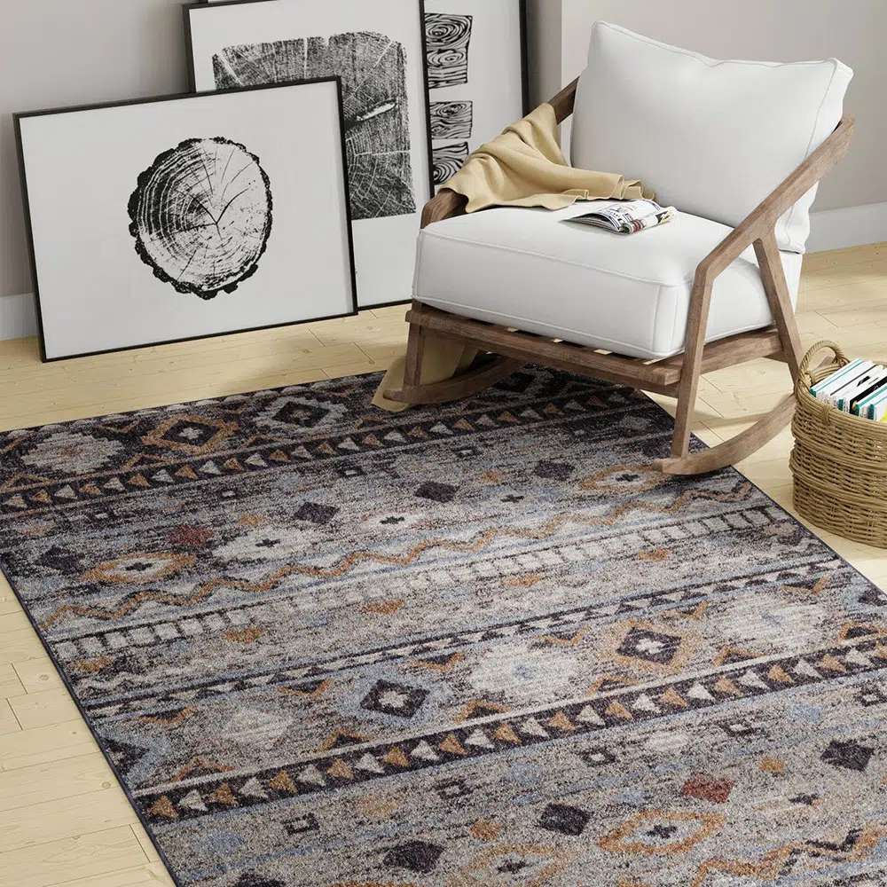 Boho Mirage Rug with geometric patterns and earthy tones, styled with a white armchair, modern art frames, and a natural woven basket on a wooden floor.