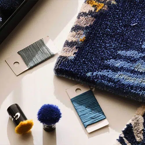 Close-up of a blue rug sample with color swatches and matching yarns, showcasing the precision and attention to detail in RugVision’s design process.