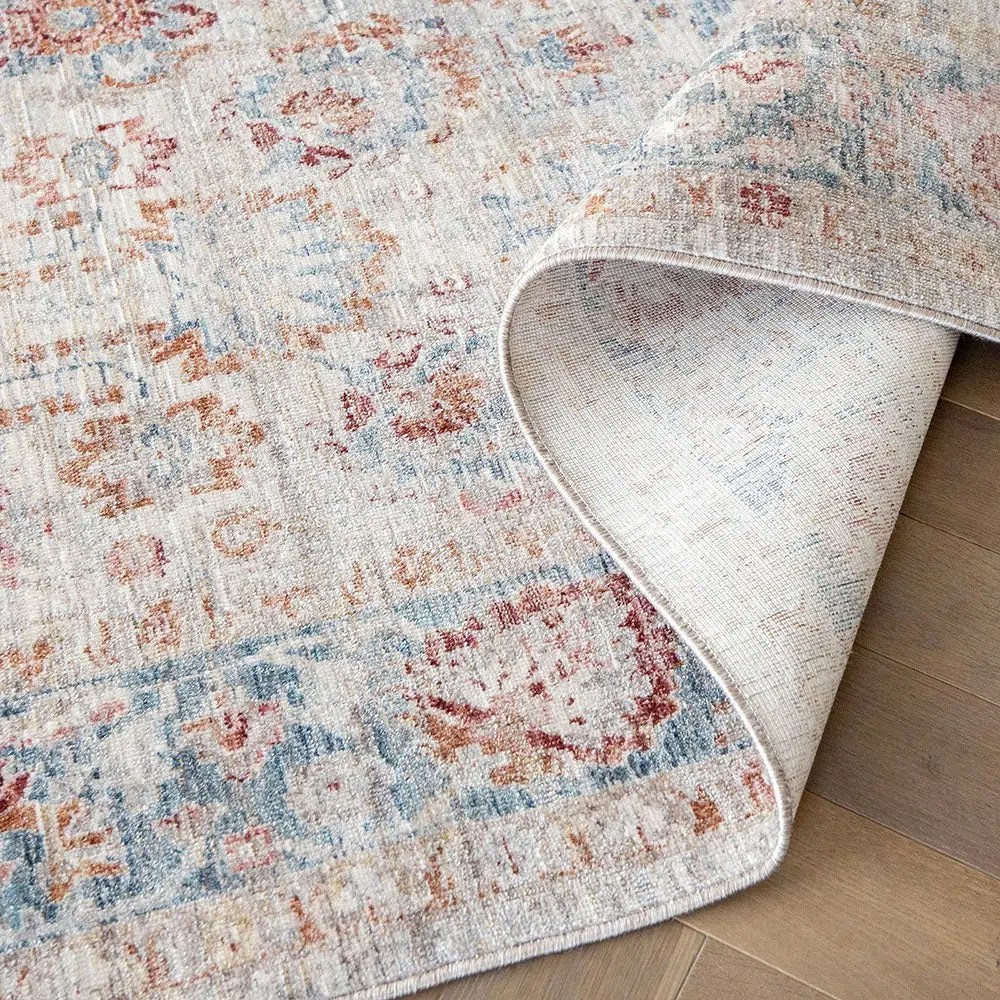 Close-up of the Bustan Rug showcasing intricate floral motifs in beige, blue, and red tones, with a soft matte texture and durable polyester backing.