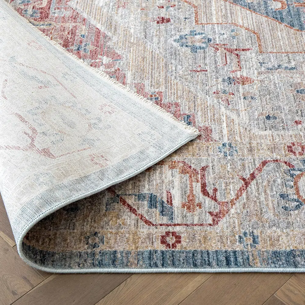 A top view of the Ishtar Medallion Rug with a folded edge, highlighting its intricate patterns and soft tones of blue, cream, and red on a modern floor setting.