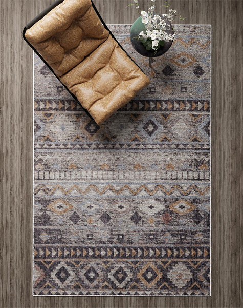 A top-down view of the Boho Mirage Rug with geometric patterns and earthy tones, styled with a tan cushioned chair and a vase with white flowers on a wooden floor.