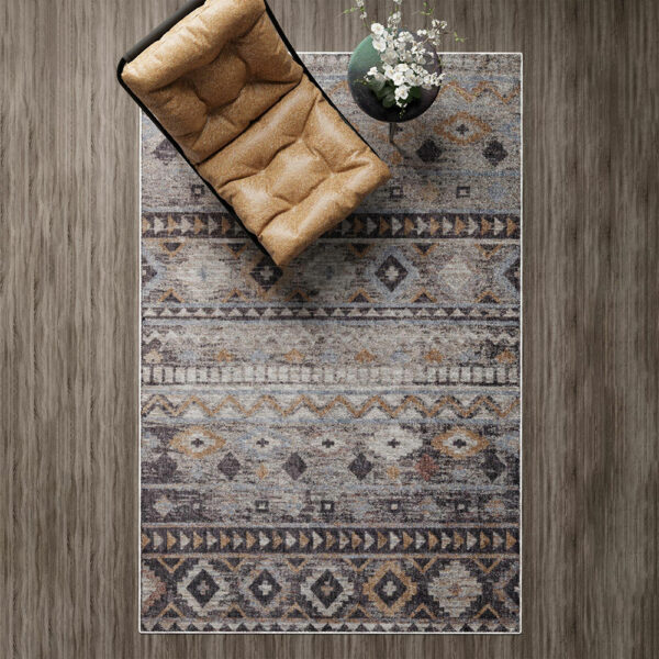 A top-down view of the Boho Mirage Rug with geometric patterns and earthy tones, styled with a tan cushioned chair and a vase with white flowers on a wooden floor.